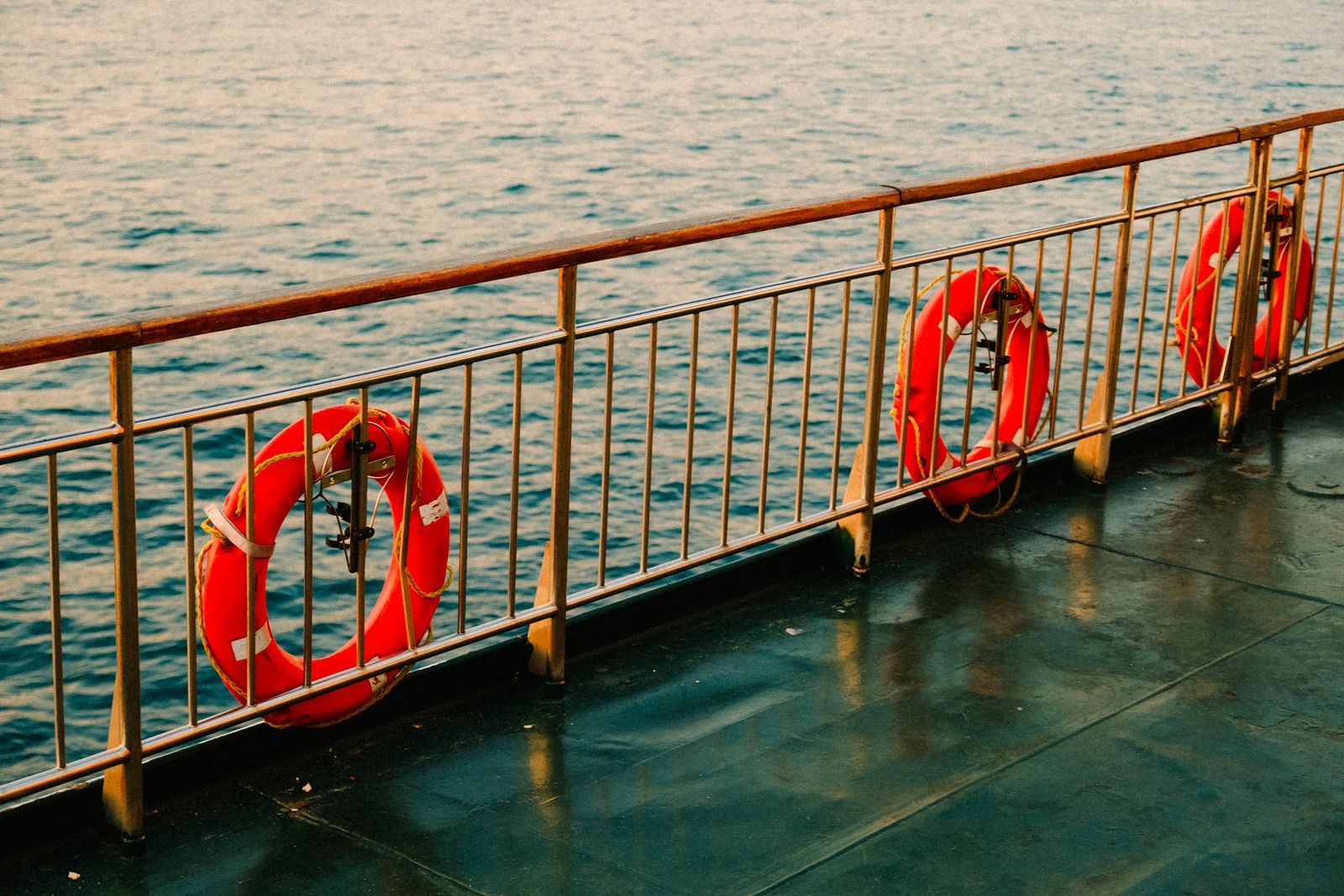 Ship deck railing with orange lifebuoys above a calm sea