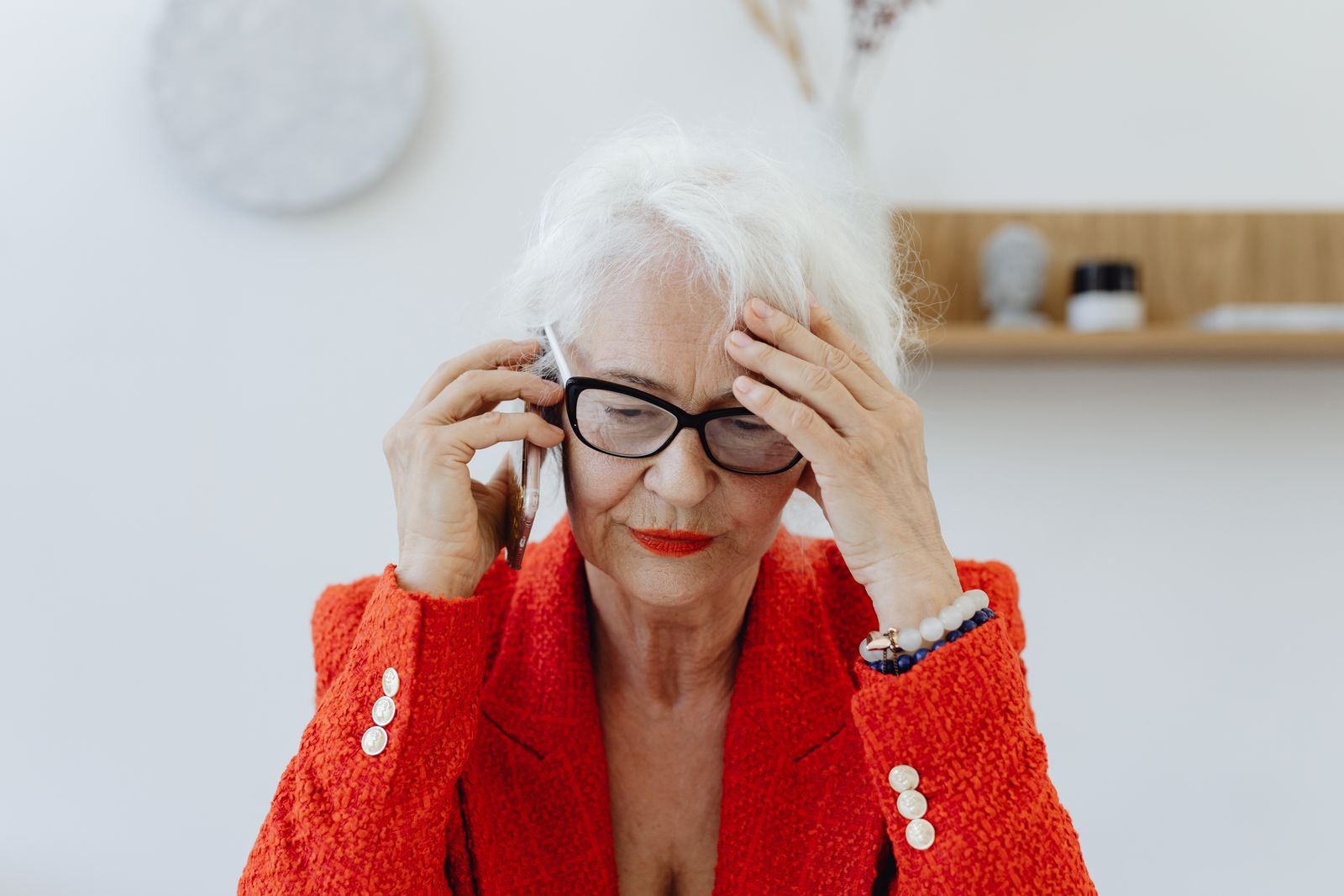 Older woman in a red jacket holding her head while on a phone call, as many do after free cruise scam calls